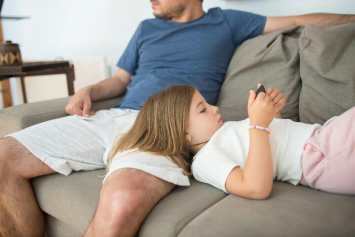 dochter bij vader op schoot, kijkt op telefoon, online pesten