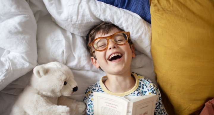 lezen voorlezen jongetje met bril lachend in bed met boek