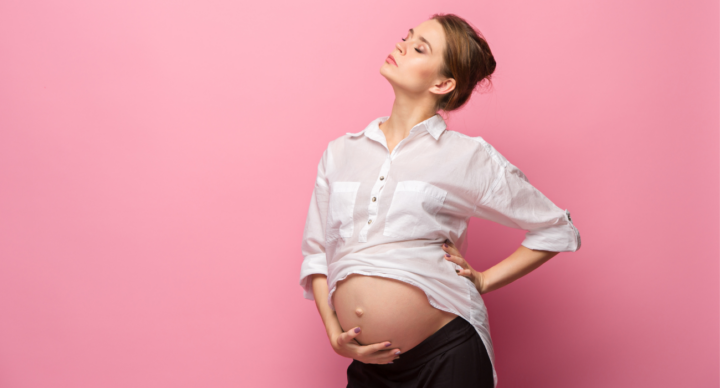 vrouw met kleding staat voor roze achtergrond met blote zwangere buik